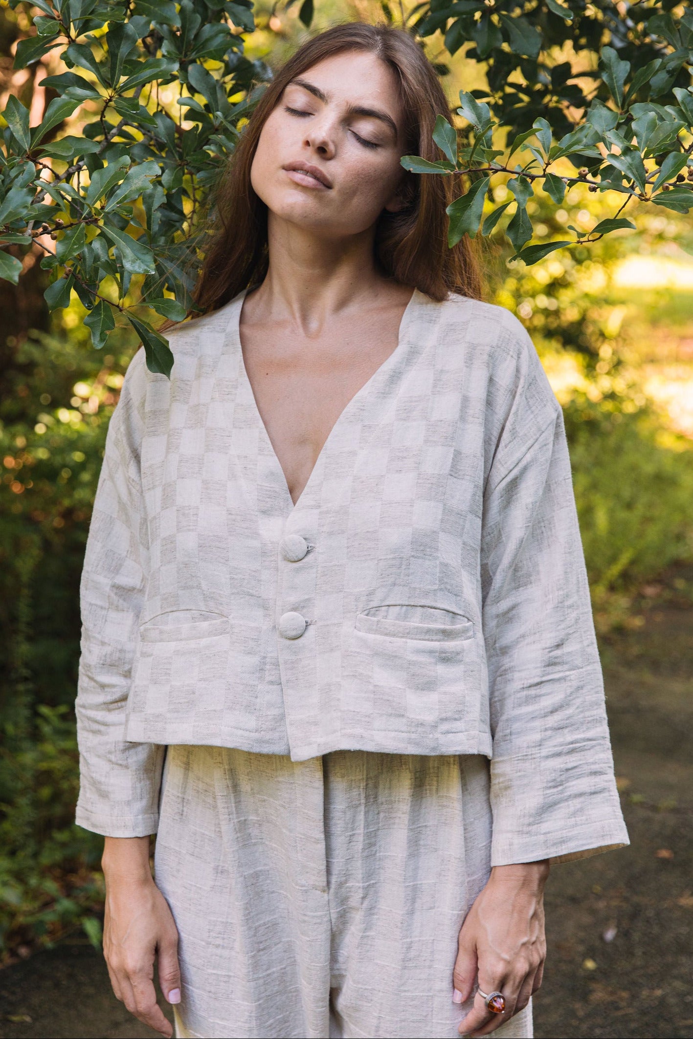 Woman in a light-colored outfit standing in a natural setting with greenery.